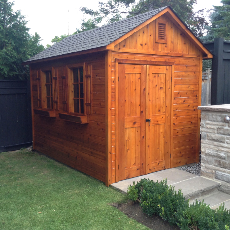 Stained cedar shed with double doors beside a stone patio