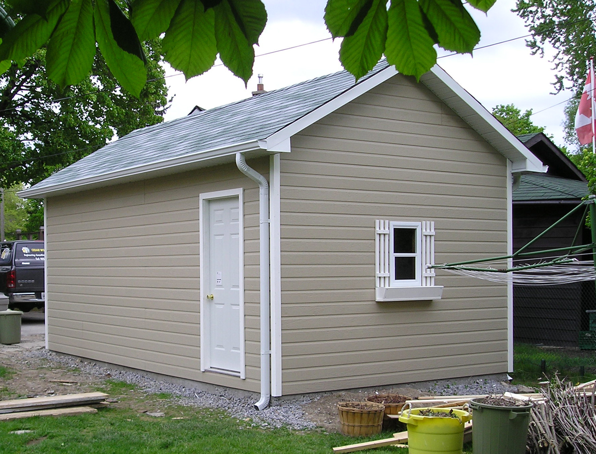 Detached outbuilding with grey siding and a shuttered window